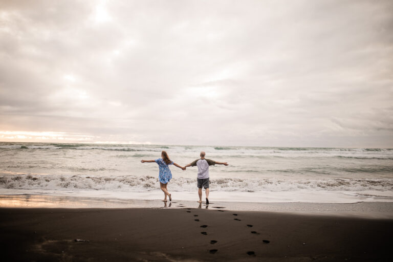 An adventurous couple hold hands and run into the ocean, at a beach near Auckland in New Zealand