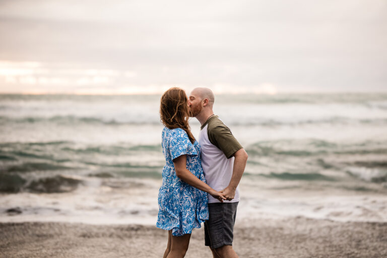 A couple share a kiss, on Piha beach in New Zealand