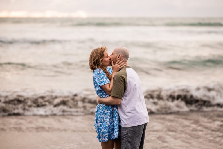 A couple share a kiss, on Piha beach in New Zealand
