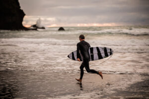 A surfer runs along the beach at Piha