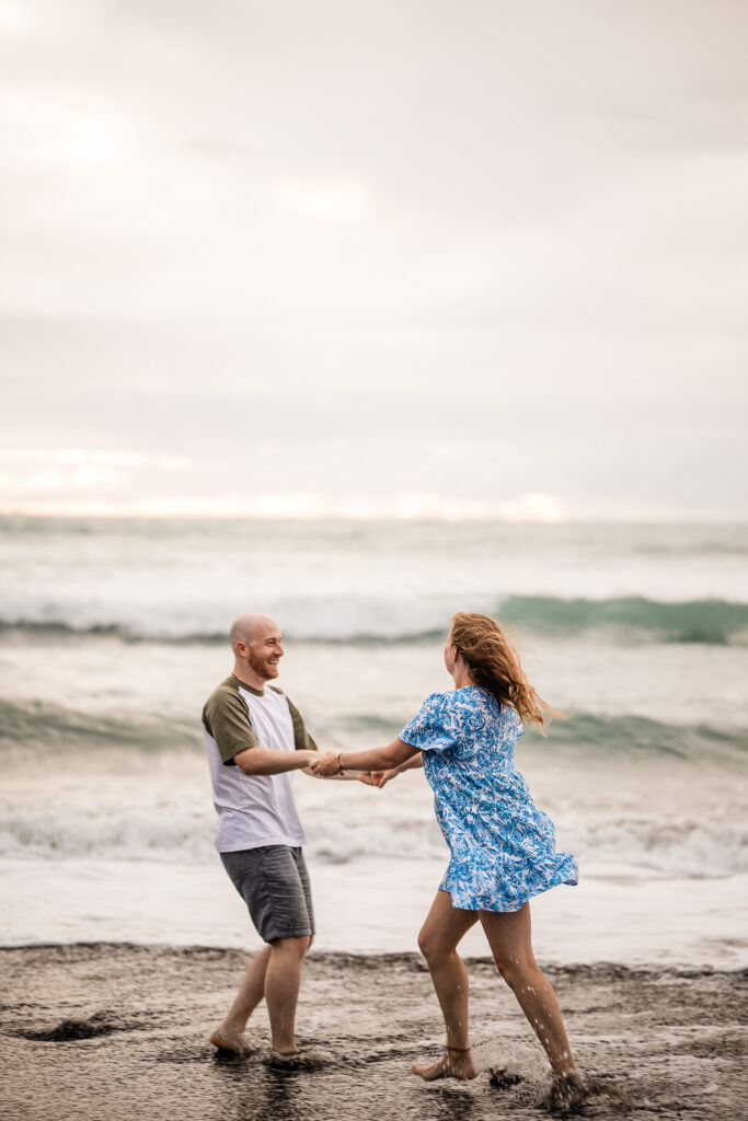 A young couple dance together in the sea during a beach pre-wedding shoot at Piha beach