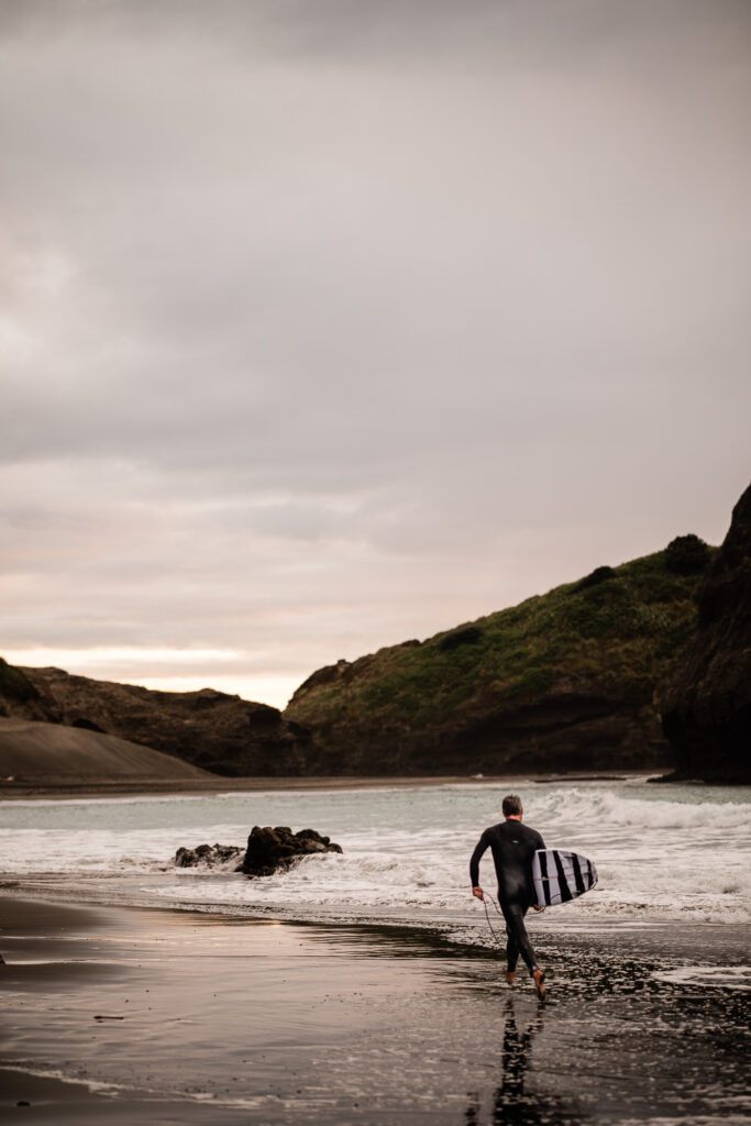A surfer runs along a windswept beach in NZ