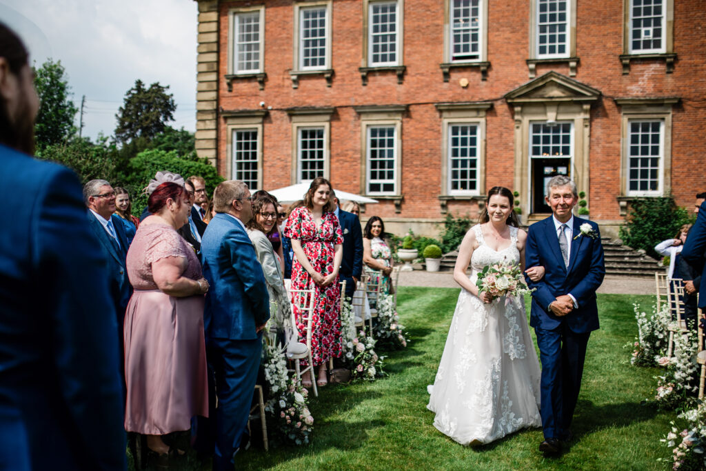 A bride walks down the aisle, during an outdoor wedding ceremony at Davenport House, by a wedding photographer UK