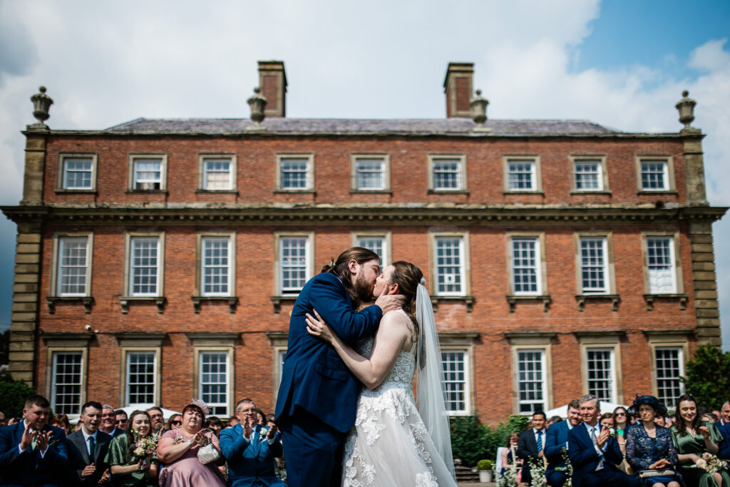 A bride and groom share their first kiss during an outdoor wedding ceremony at Davenport House