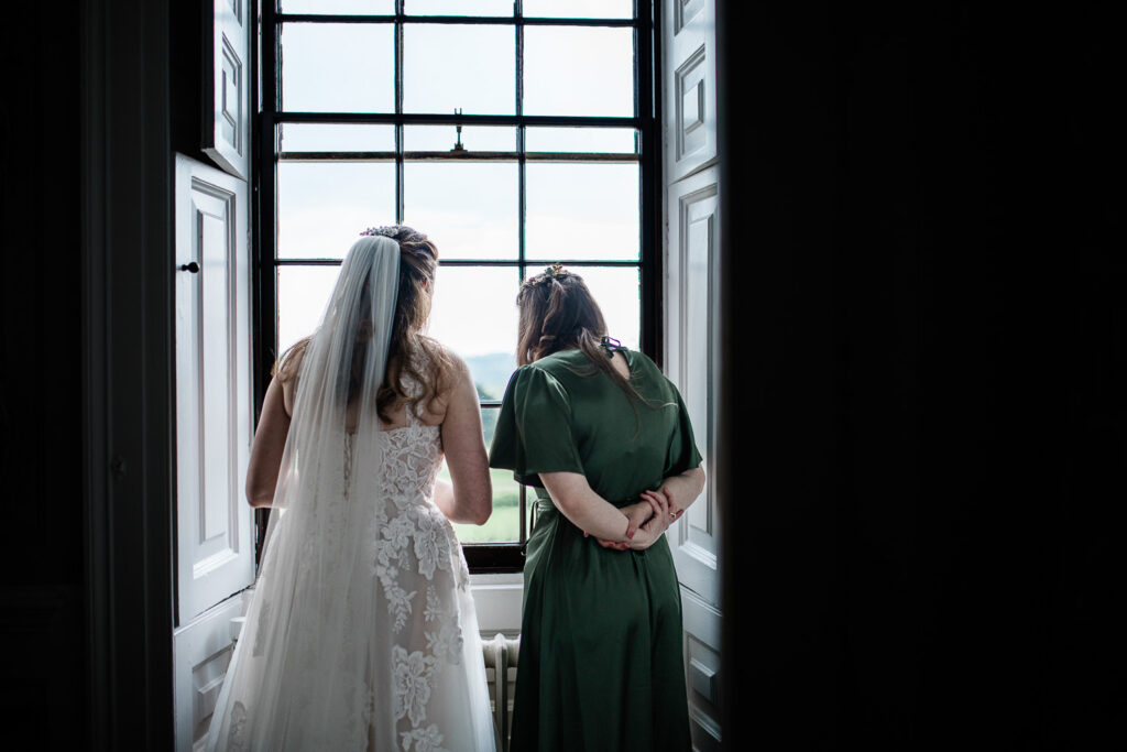 A bride and her maid of honour look out the window, before the wedding ceremony