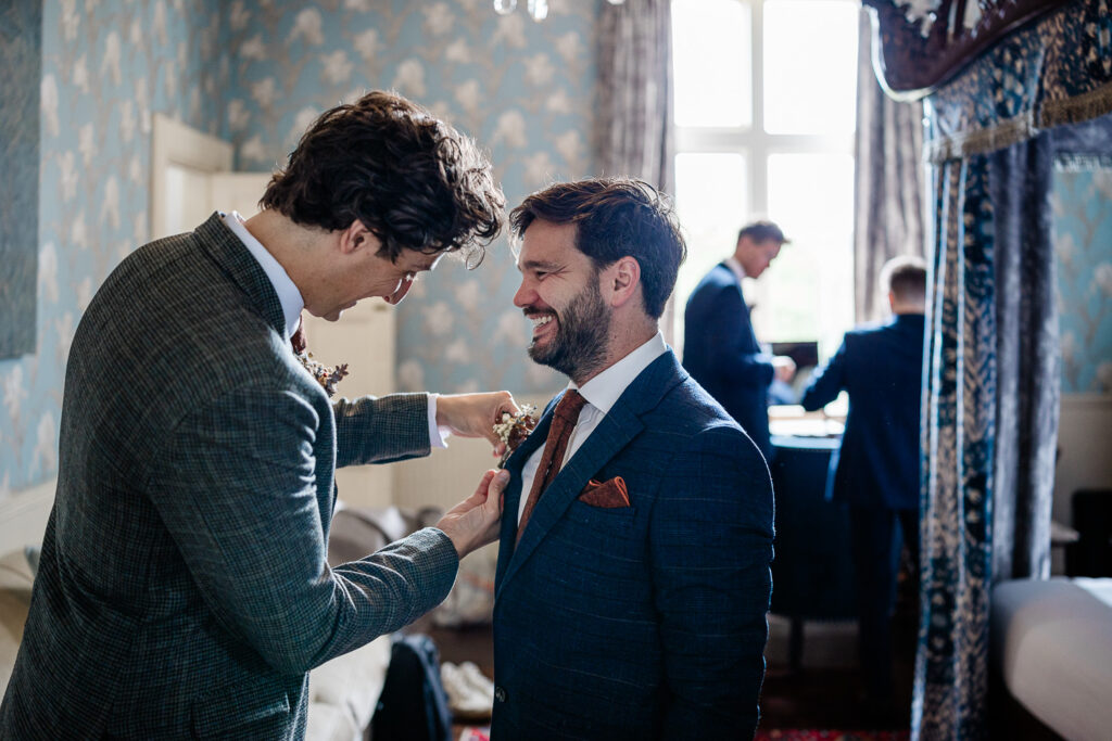 a groom pins a corsage onto his best man, captured by a wedding photographer at huntsham court