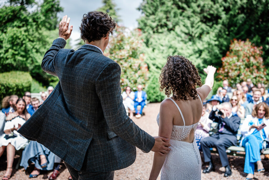 a bride and groom wave to their guests at the end of a ceremony