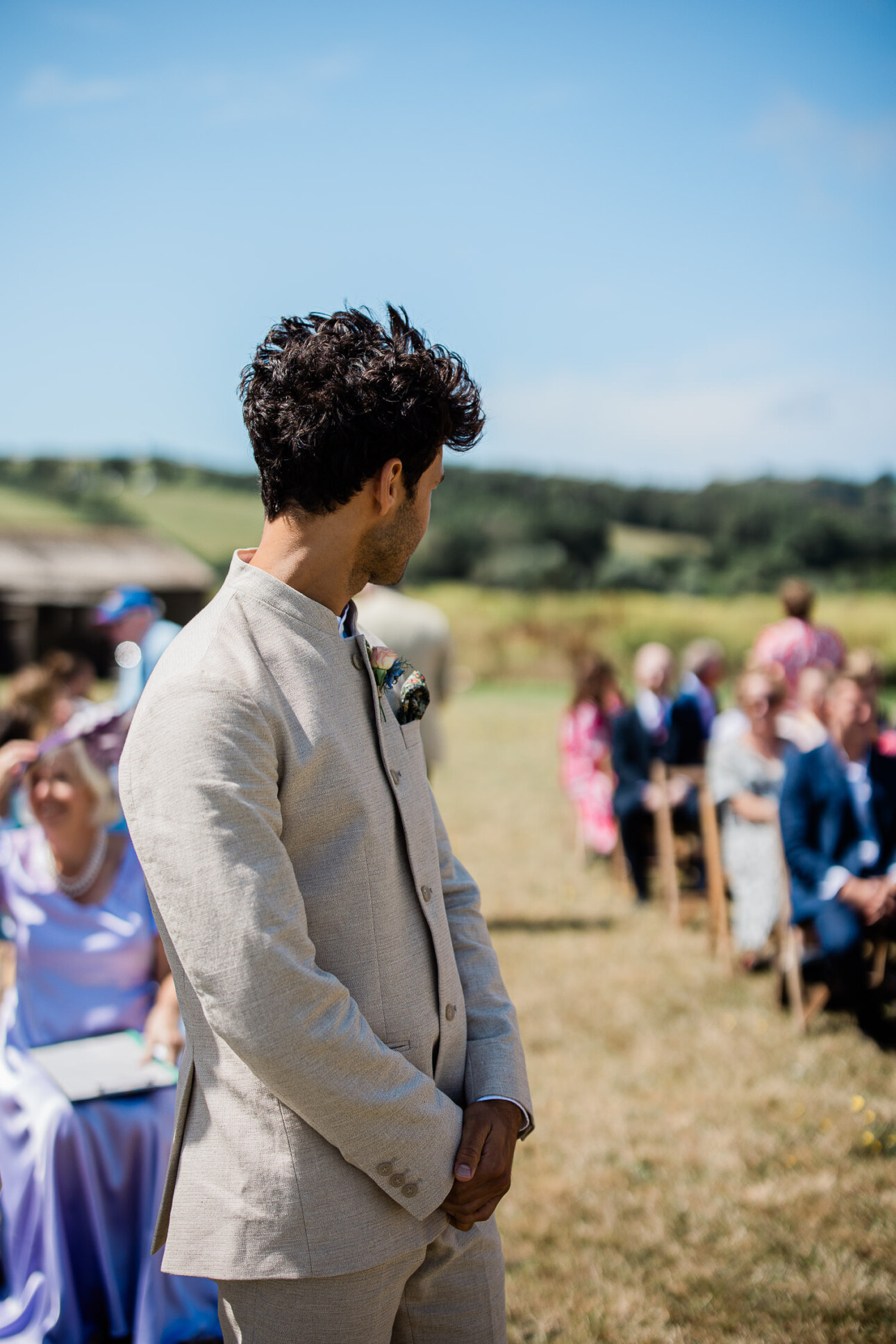 A groom looks down the wedding aisle of an open-air wedding ceremony, waiting for the boho bride to arrive.