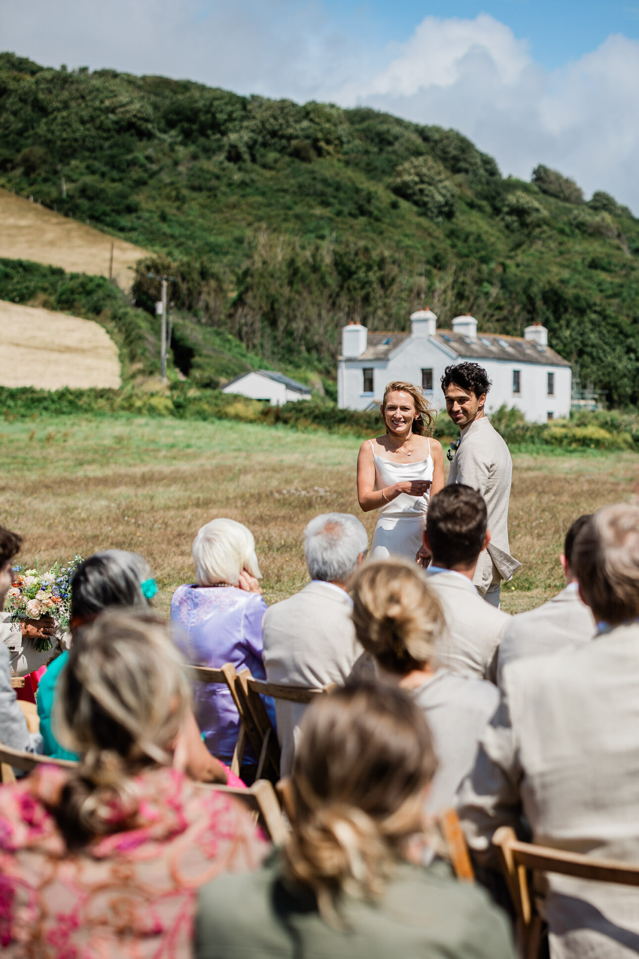 A bride and groom turn around to laugh at something one of the guests has said, during an open-air ceremony in the english summertime.