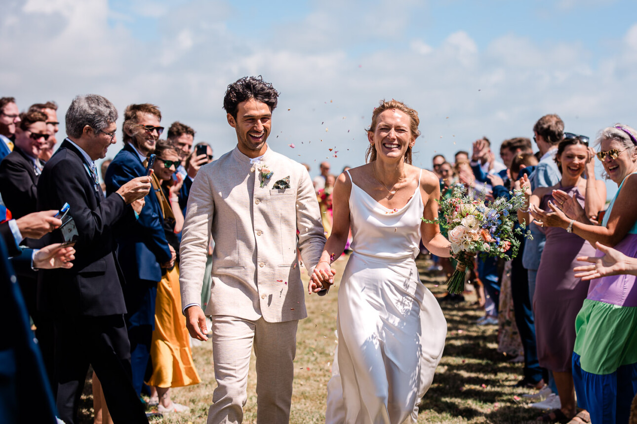 A newly married couple grin in excitement, during an open-air confetti shot in the summertime.