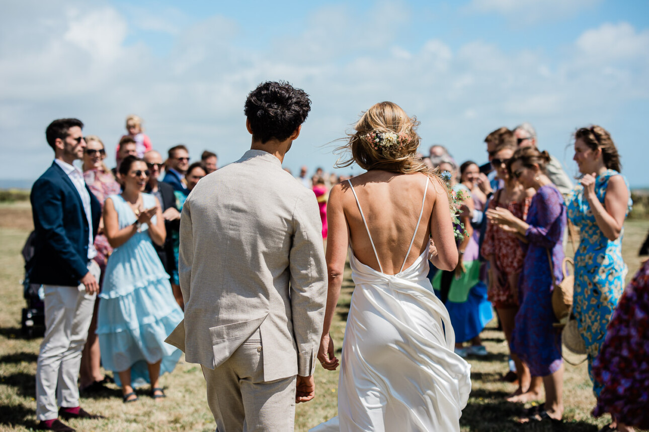 A bride and groom look back at their wedding guests at their bohemian inspired seaside wedding, after an outdoor confetti shot.
