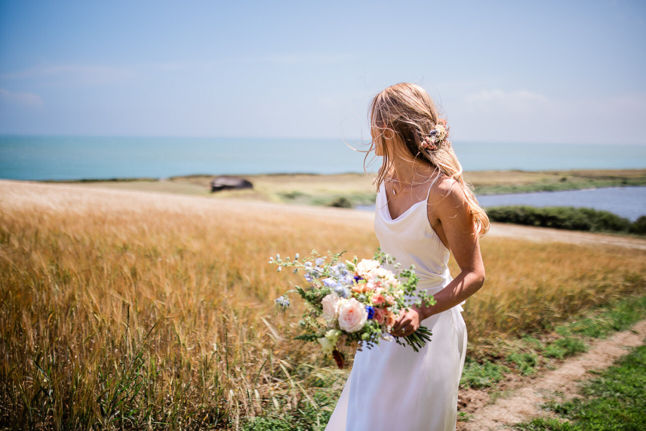 A bride looks back over the Devonshire hills to see her outdoor wedding ceremony location by the sea.
