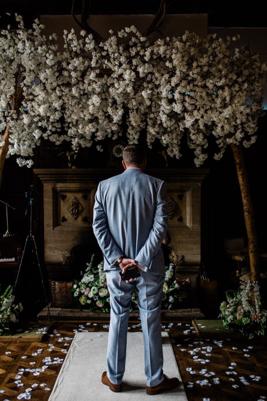 A groom stands nervously at the top of the aisle at Huntsham Court, waiting for the bride.