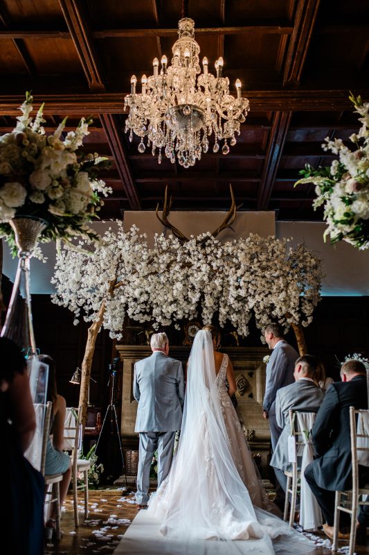 A bride and her father stand at the top of the aisle during a luxury wedding ceremony at English stately home wedding venue in Devon.