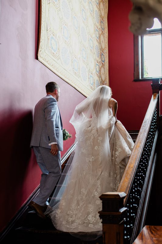 A picturesque documentary moment where a bride and groom walk up the historic staircase of an English manor house.