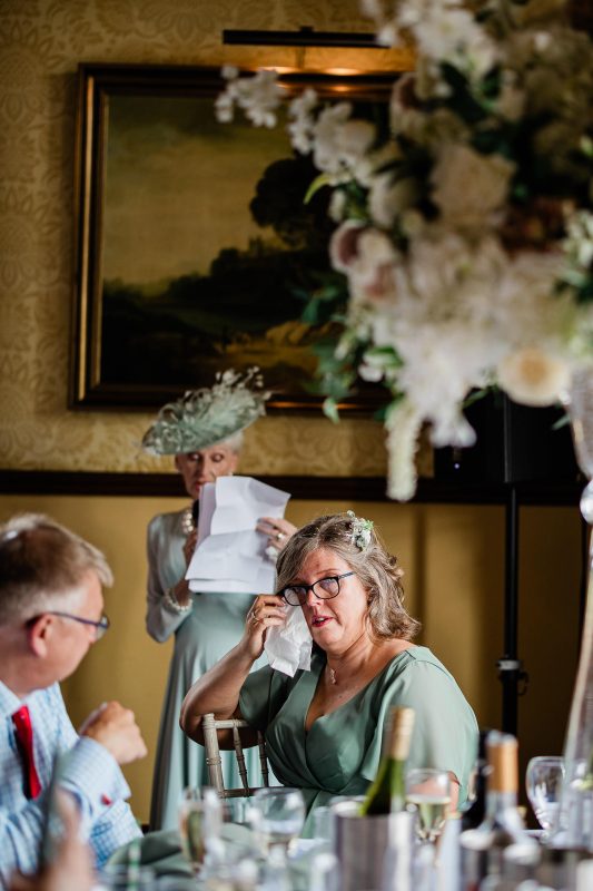 A candid moment where a bridesmaid wipes her eyes as a mother of the bride gives a heartfelt and emotional speech.