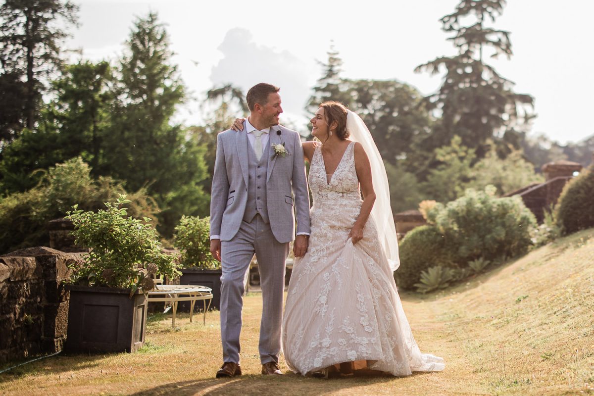 A groom and bride exchange a loving look whilst walking in country house gardens during a Huntsham Court wedding photography session.