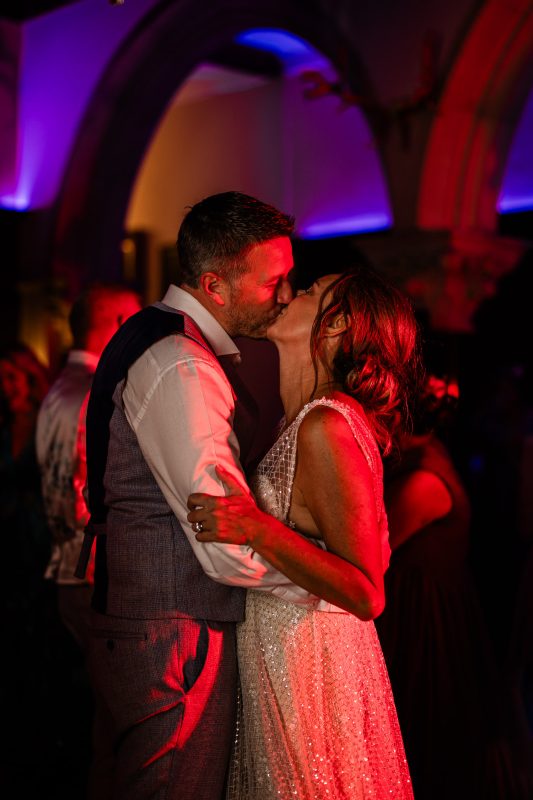 A bride and groom exchange a kiss under the arches of historic wedding venue, during the evening party.
