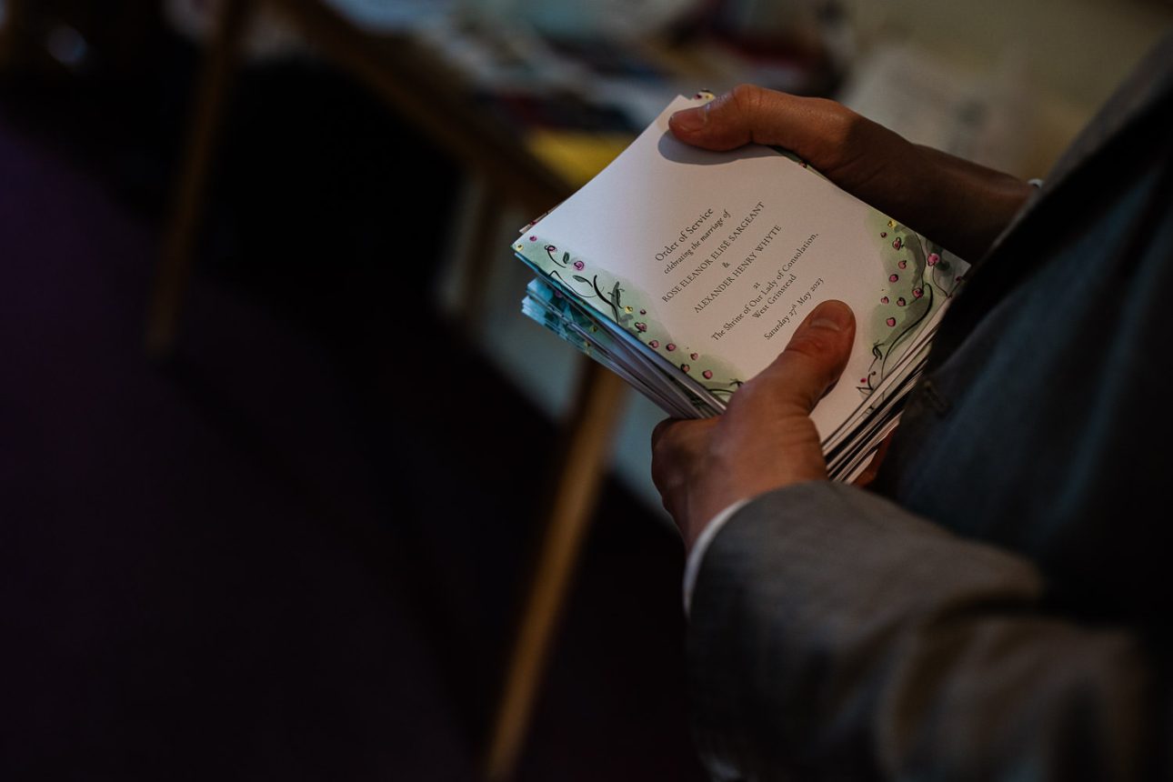 A wedding guest reads the order of service before an English church ceremony.