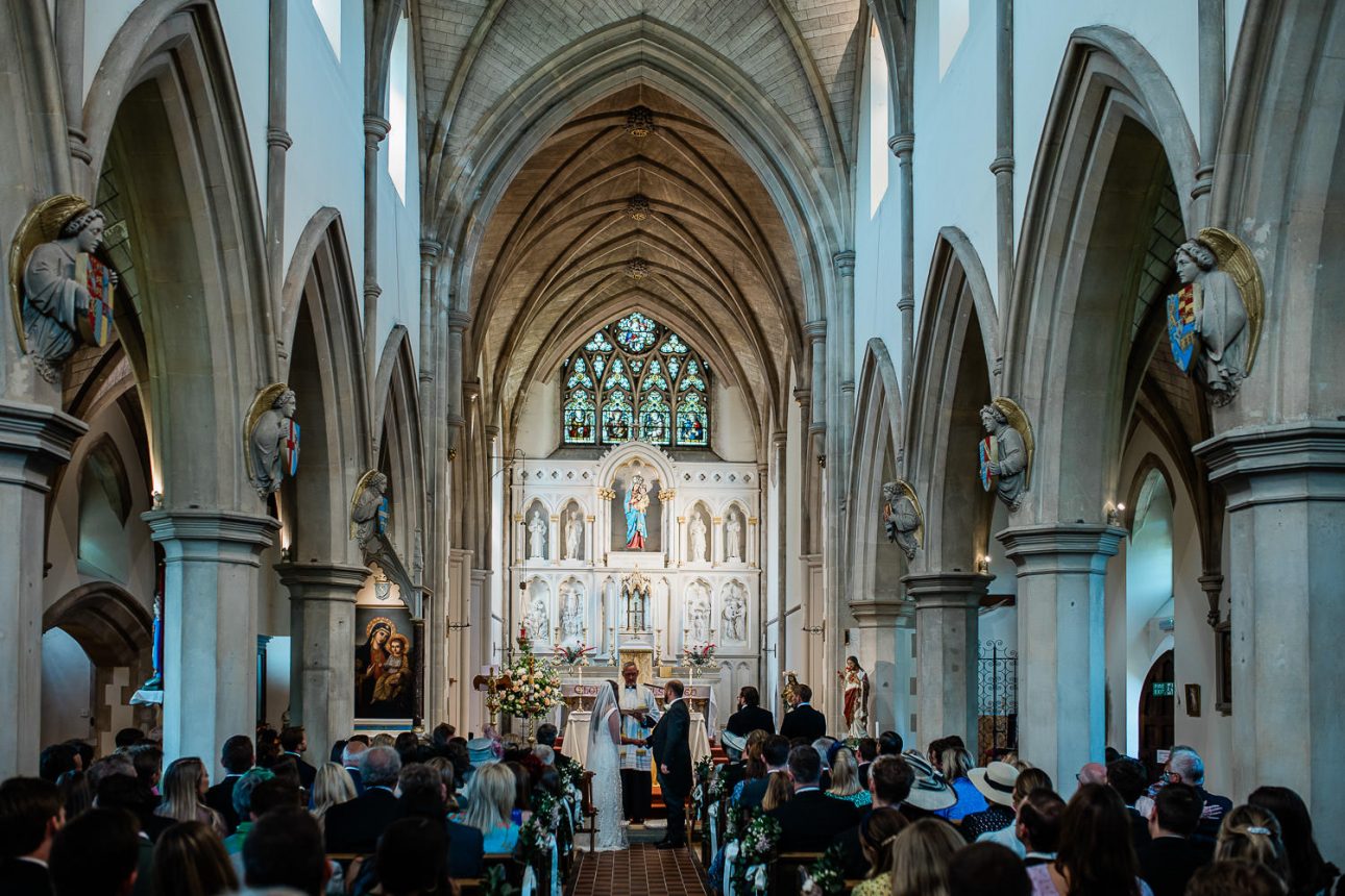 The groom and bride say their wedding vows at the top of the aisle, in a historic church in England.