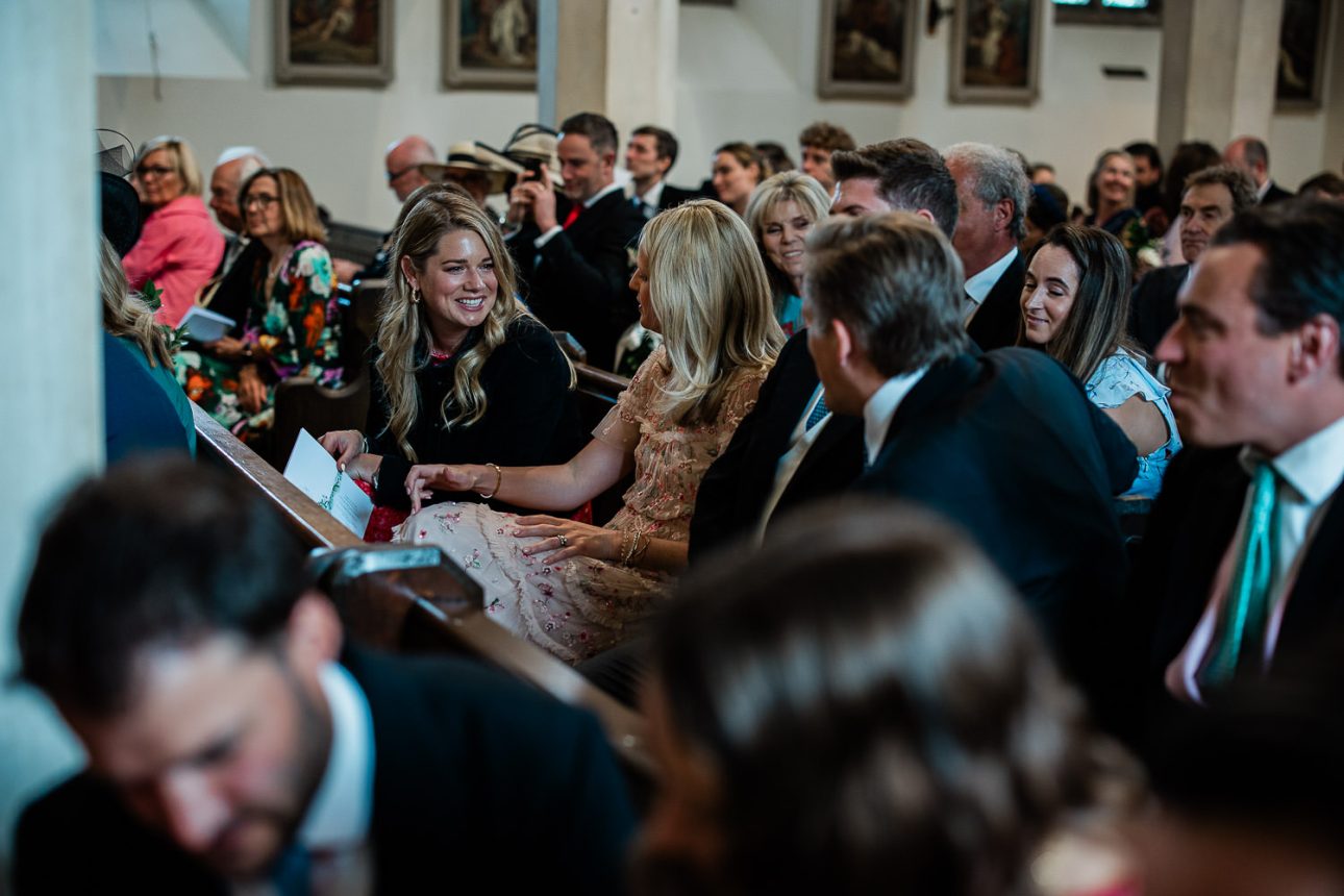 Two wedding guests exchange a joke, during a religious wedding ceremony in West Sussex.