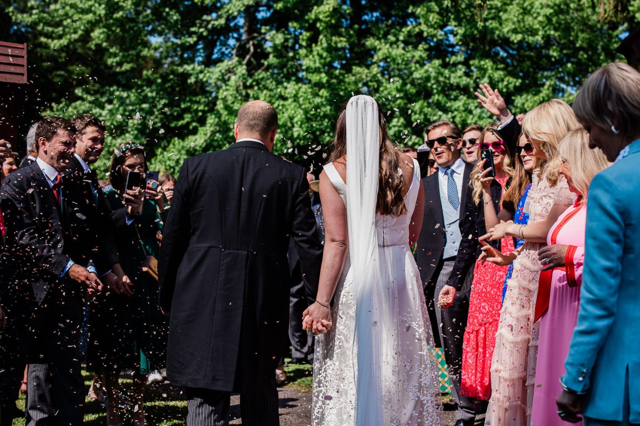 Newly weds are cheered on by their friends and family during confetti shot at summer wedding in Sussex.