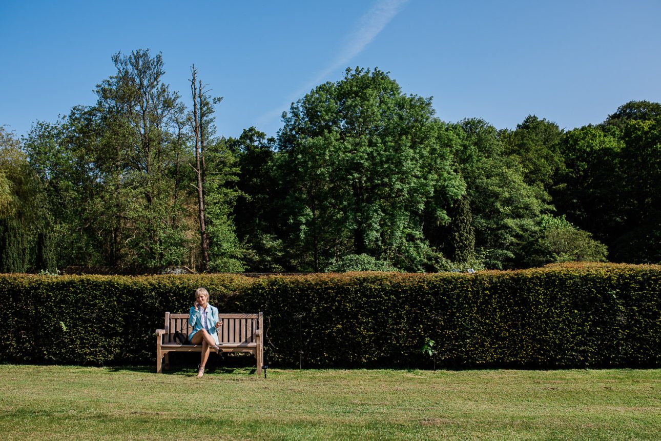 A candid moment of a wedding guest relaxed on a bench, in the english gardens at Slaugham Place.