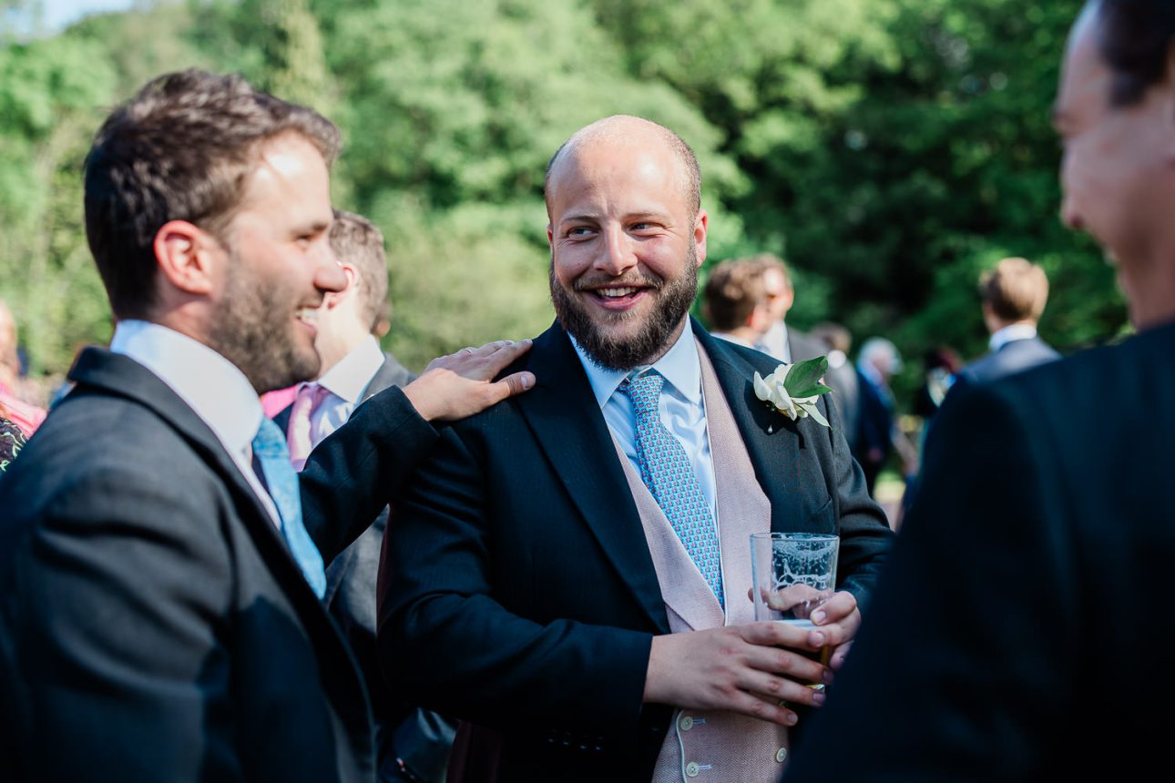 A candid moment of a groom laughing with a groomsman, during an outdoor wedding reception.