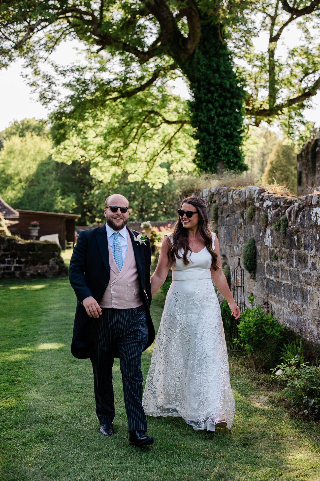 A groom and bride walk together, wearing matching sunglasses.
