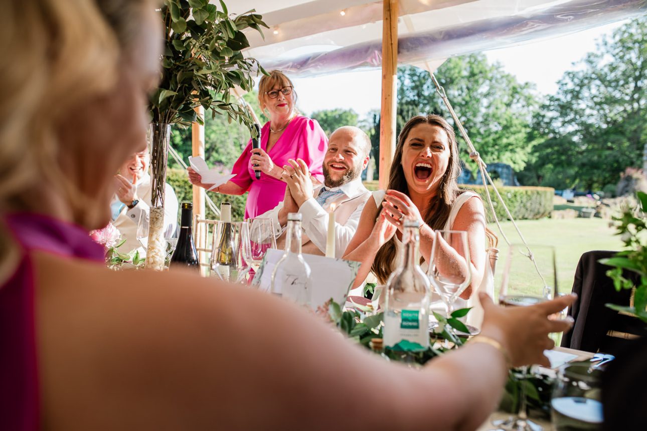 Typical reportage photography moment where bride, groom and mother of the bride are cracking up laughing at a wedding speech.
