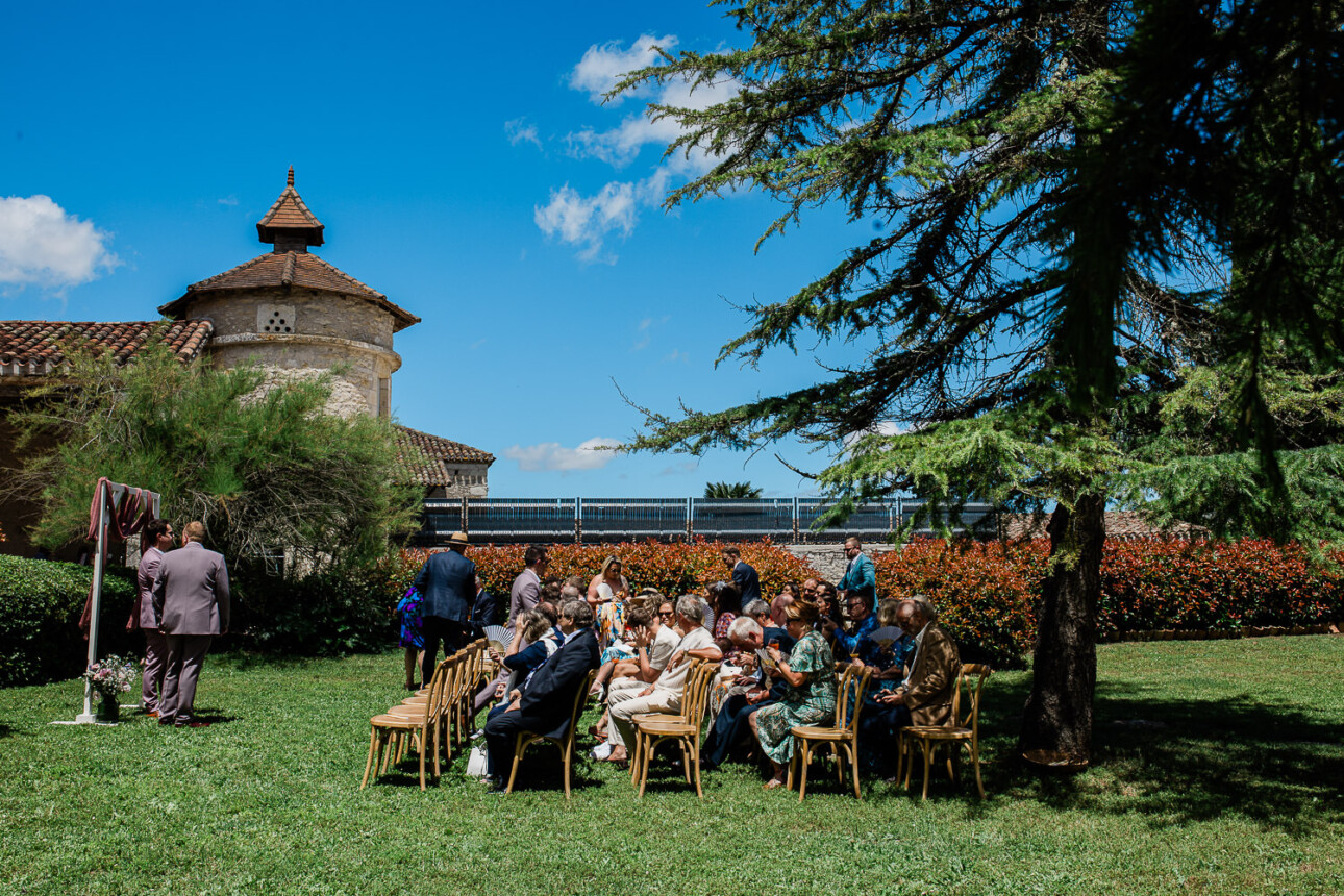Guests sit at an outdoor ceremony at a french chateau, waiting for the bride to arrive.