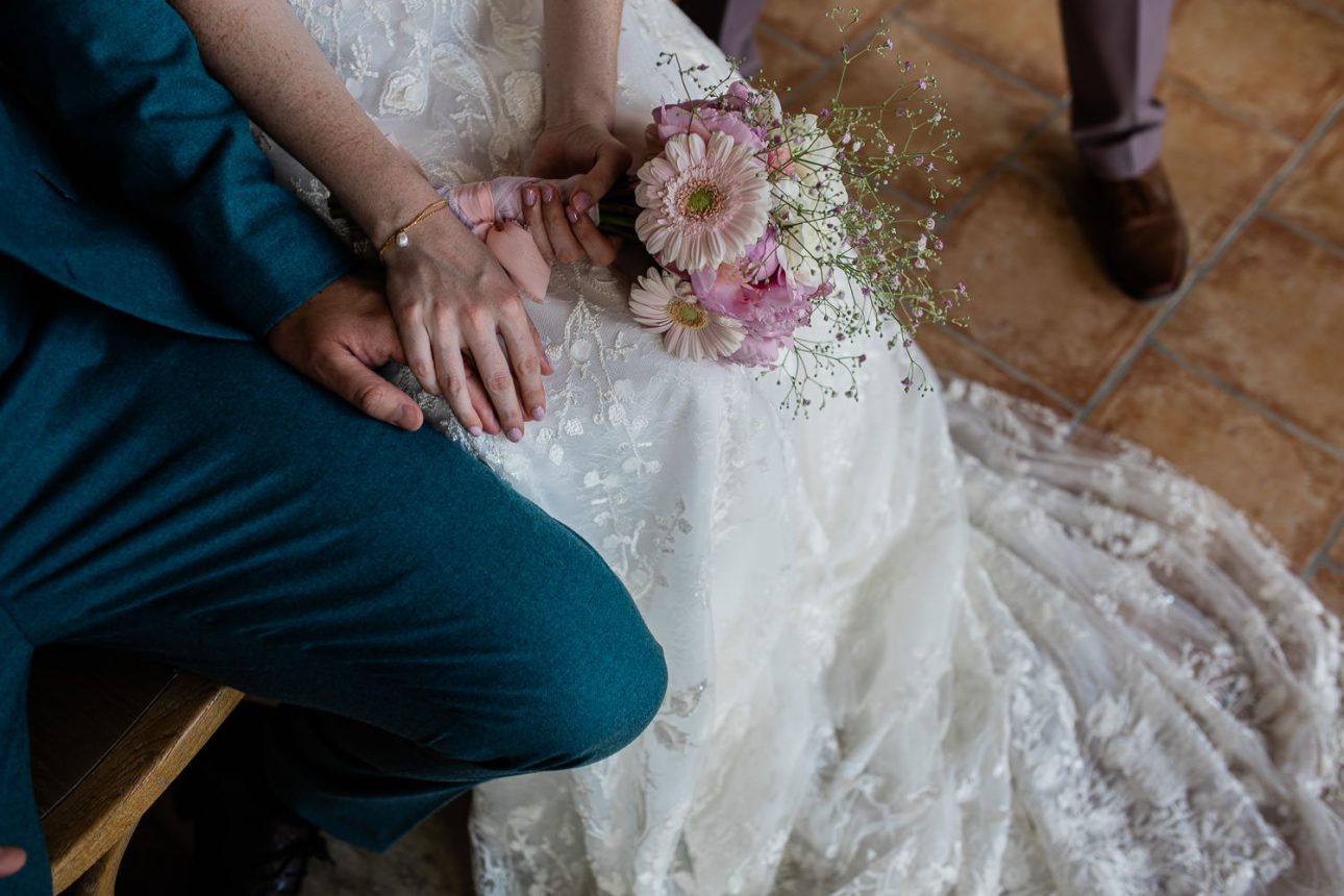 A candid moment of a bride and groom holding hands, during group formals at a wedding.
