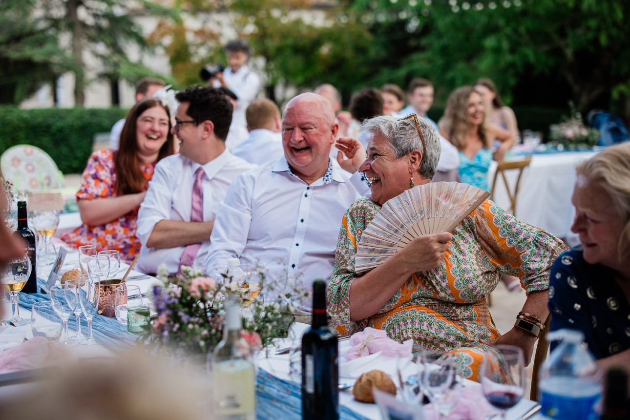 Wedding guests laugh excitedly at a funny speech, during an open air reception in France.