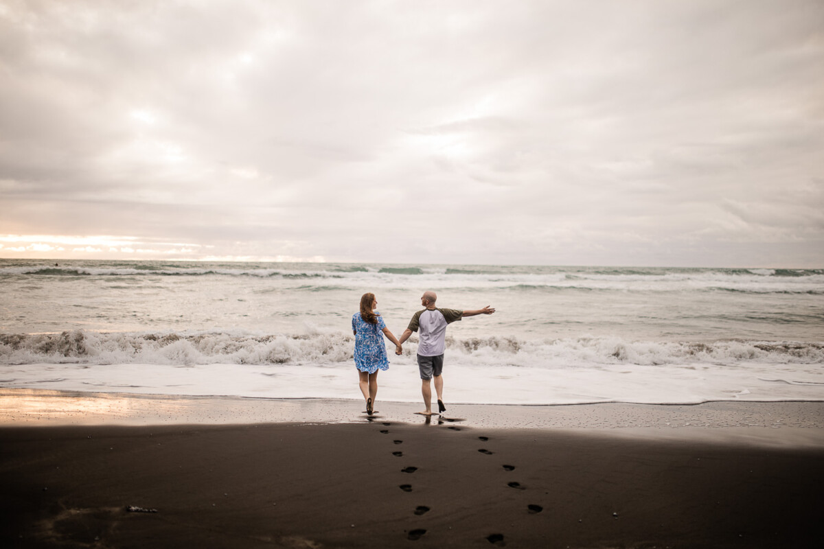 An adventurous couple hold hands and run into the ocean, at a beach near Auckland in New Zealand