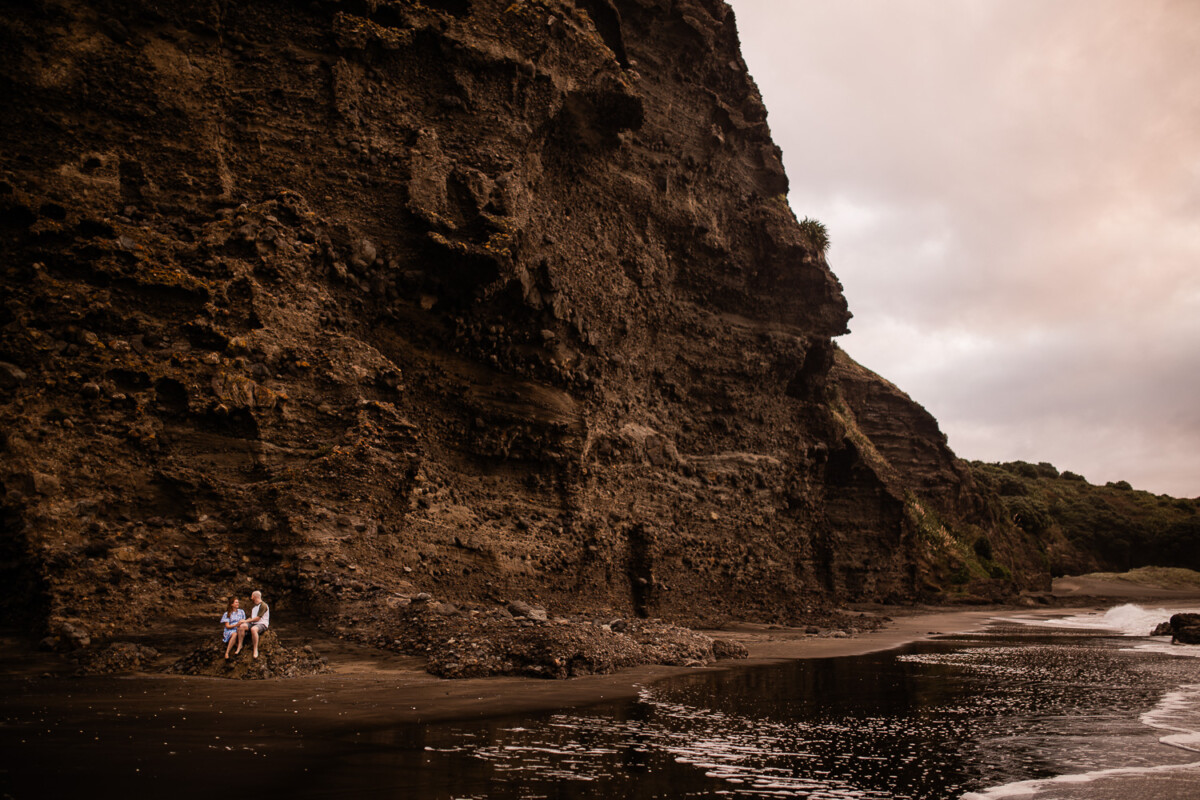 A young couple embrace on the rocks at Piha beach on the north island of New Zealand