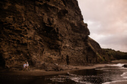 A young couple embrace on the rocks at Piha beach on the north island of New Zealand