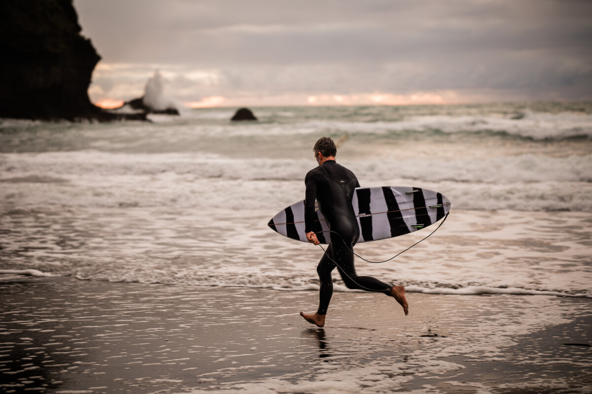 A surfer runs along the beach at Piha