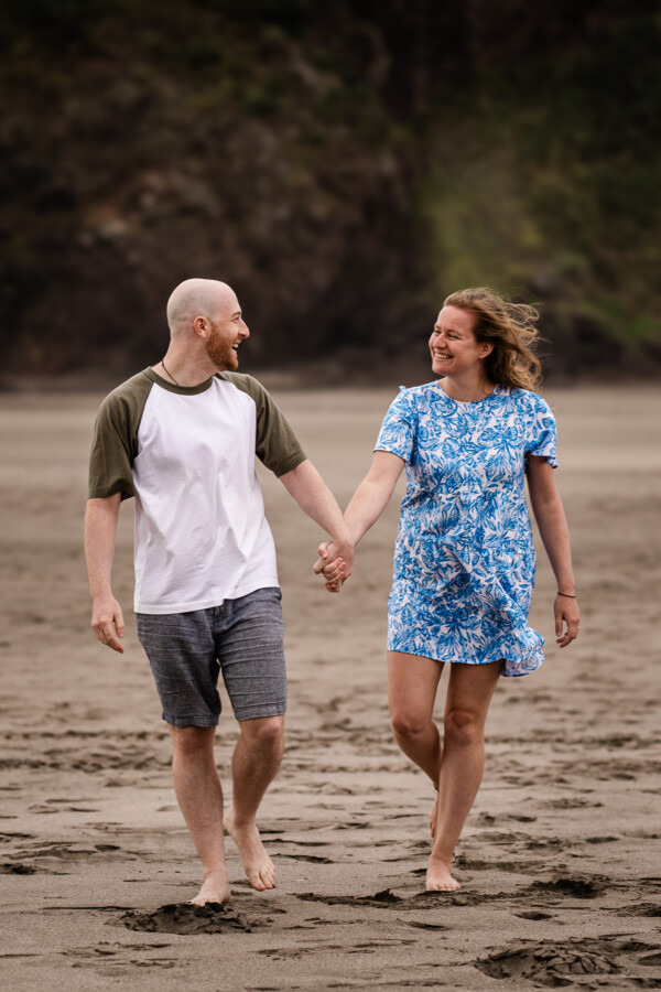 A young couple in their twenties smile at each other, during a destination photography engagement shoot in New Zealand