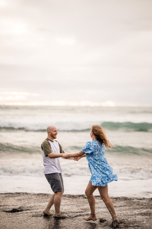 A young couple dance together in the sea during a beach pre-wedding shoot at Piha beach