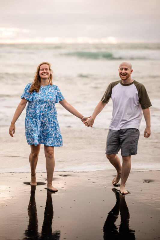 A couple smile together during a documentary wedding photography engagement shoot at Piha beach