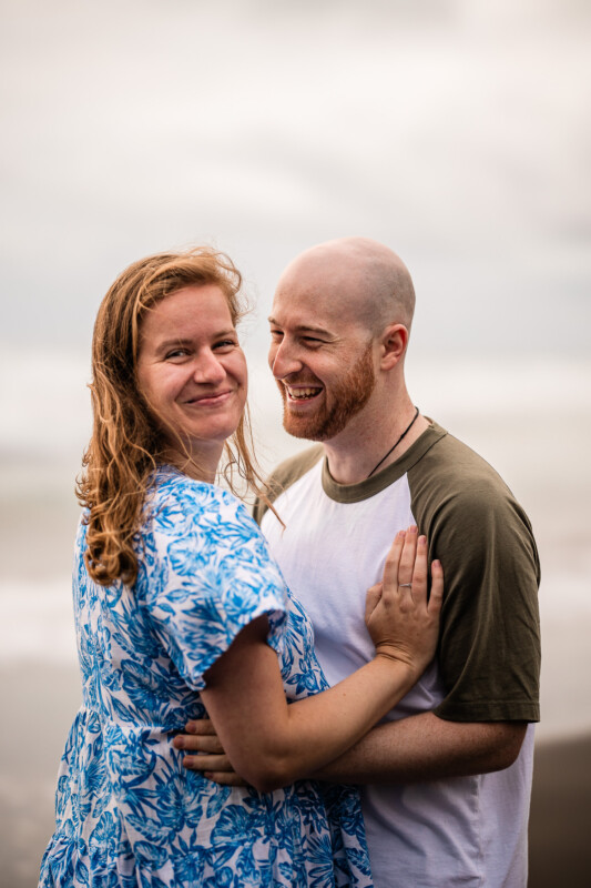 A young couple laugh together, during a documentary photography photoshoot at a beach in New Zealand