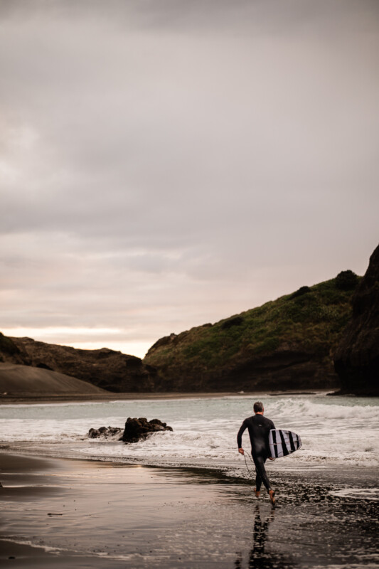 A surfer runs along a windswept beach in NZ