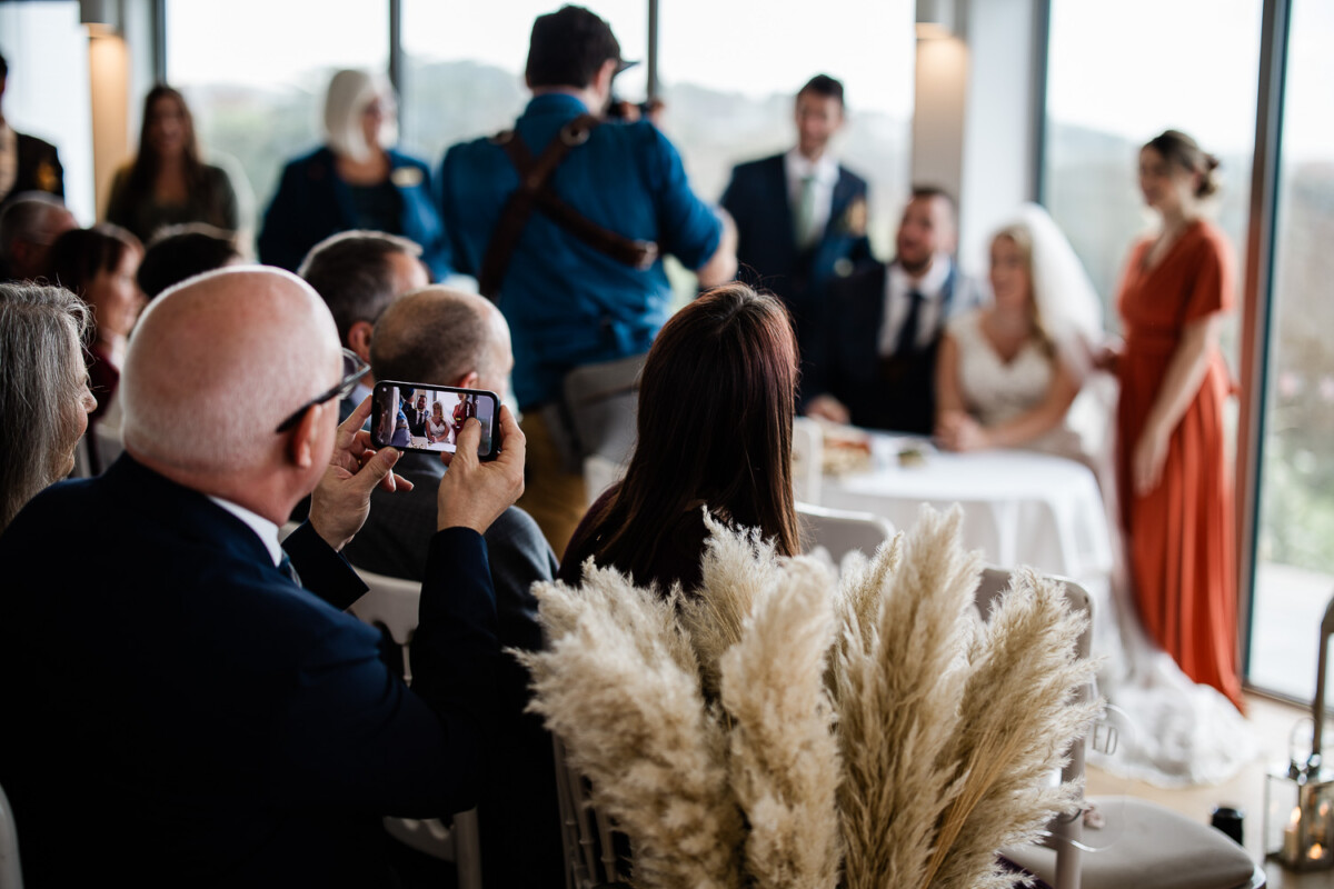 A documentary style capture of wedding guest taking a photo of the bride and groom at the registry