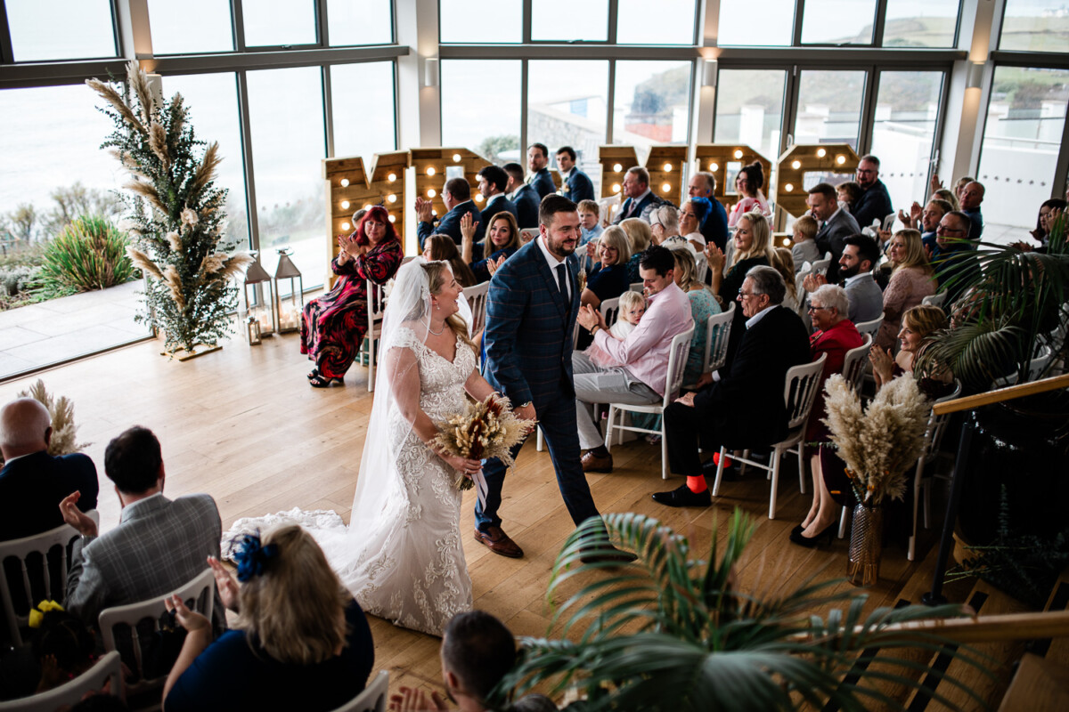 A bride and groom walk up the aisle after their wedding ceremony at Polurrian on the Lizard wedding venue in the South West