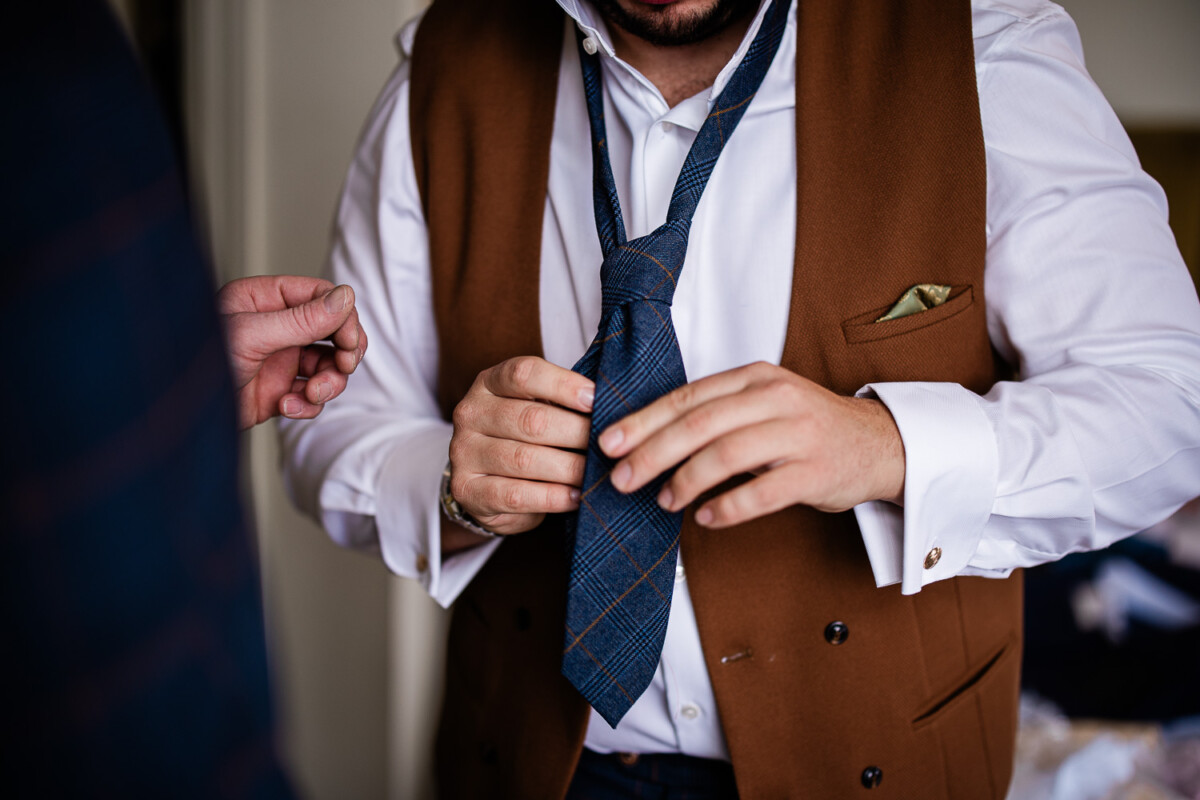 A groom does up his tie before his Cornish wedding