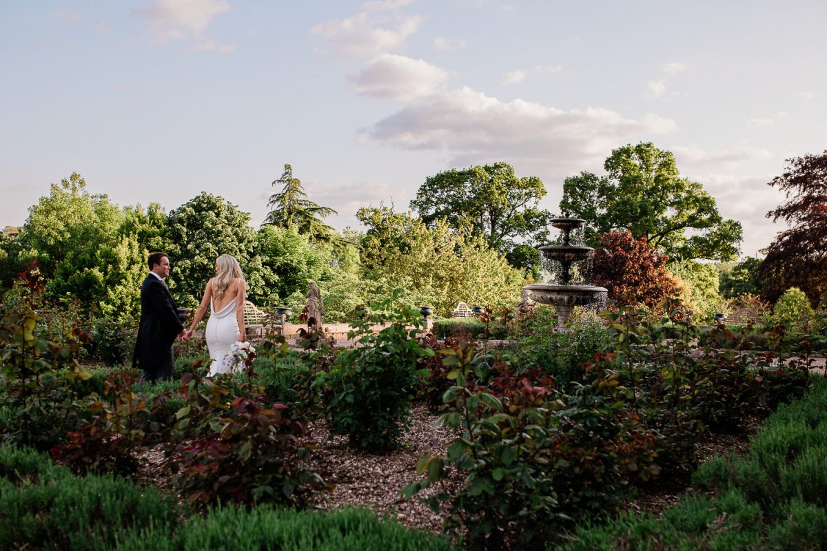 A couple walk through the stately home gardens of a Devon wedding venue
