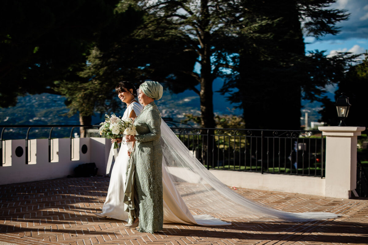 A bride walks to the wedding ceremony with her mother, doing a destination wedding in France by a wedding photographer UK