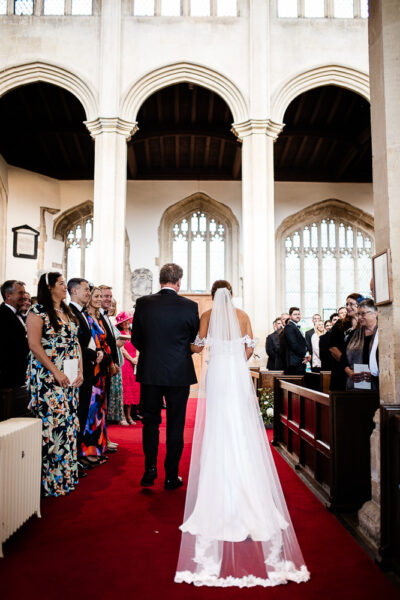 Cotswolds wedding photographer capture of a bride walking down the aisle