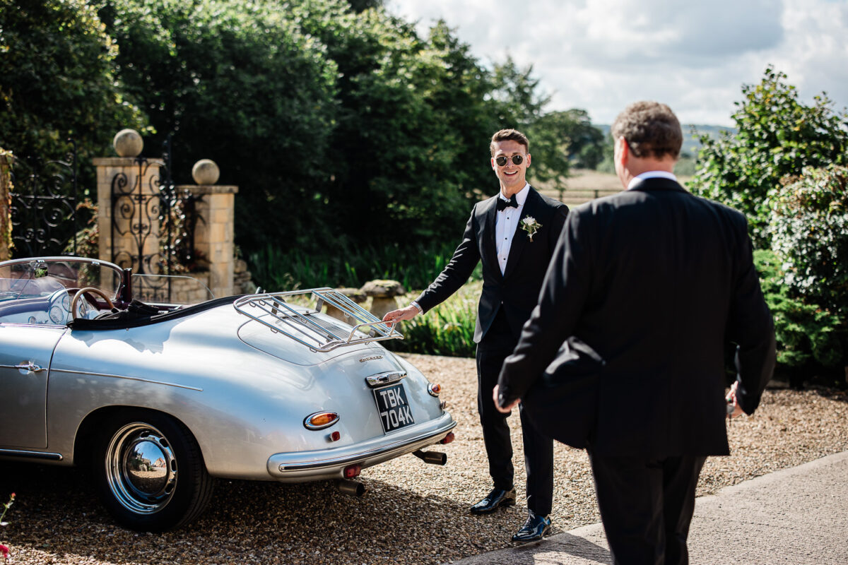 A groom gets into a vintage wedding car, during this Cotswolds wedding