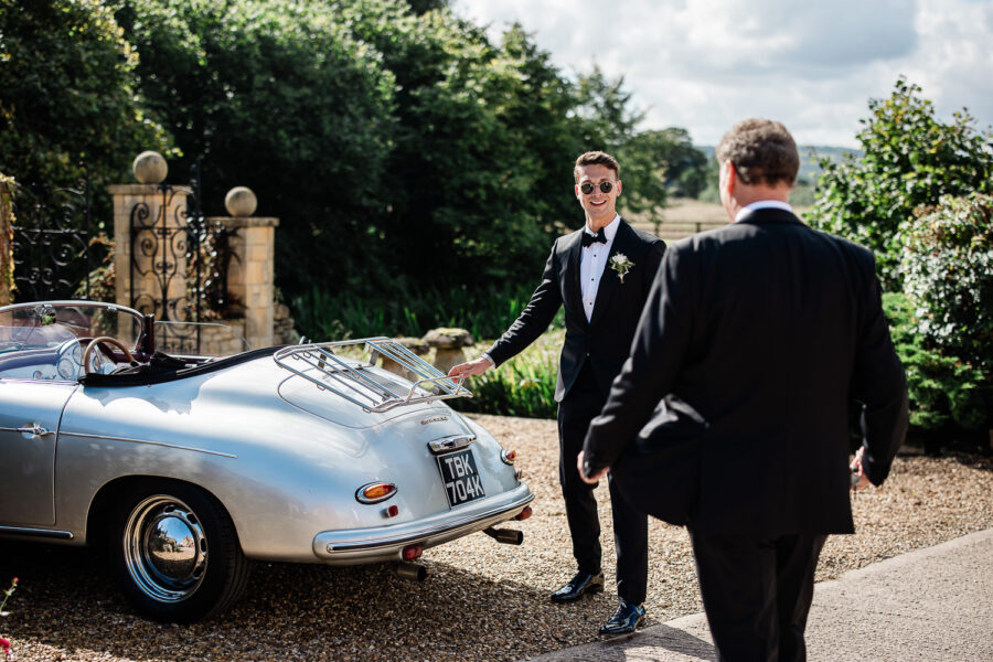 A groom gets into a vintage wedding car, during this Cotswolds wedding